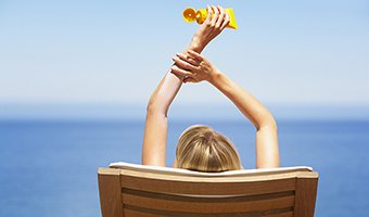 Woman at the beach holding sunscreen.