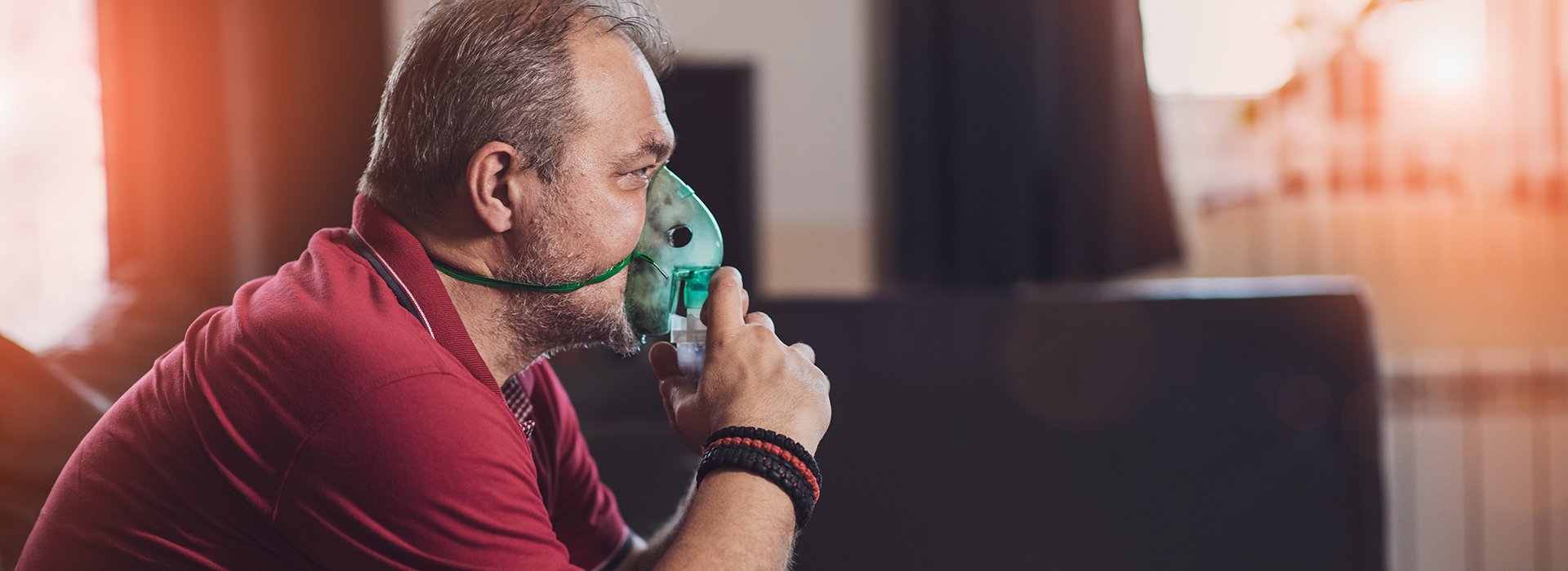 Man sitting at home wearing an oxygen mask.