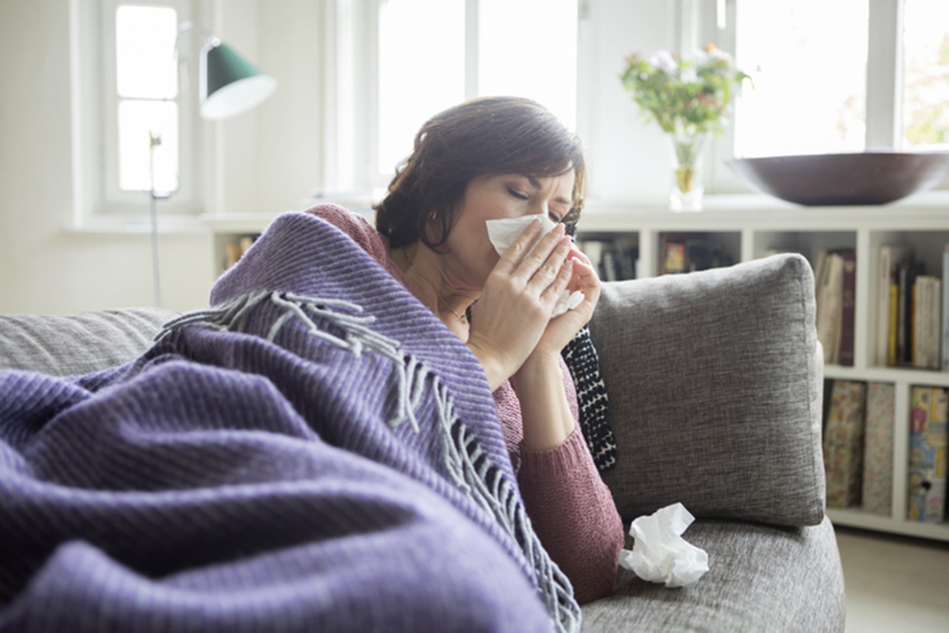 Woman on the couch sneezing.