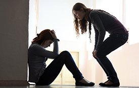 Woman sitting on the floor with another woman talking to her.